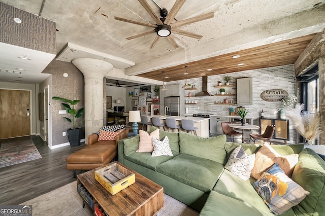 living room featuring brick wall, baseboards, ceiling fan, decorative columns, and wood finished floors