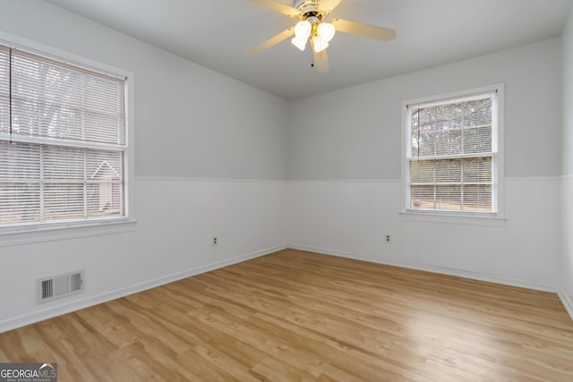 spare room with light wood finished floors, visible vents, a ceiling fan, and a wainscoted wall