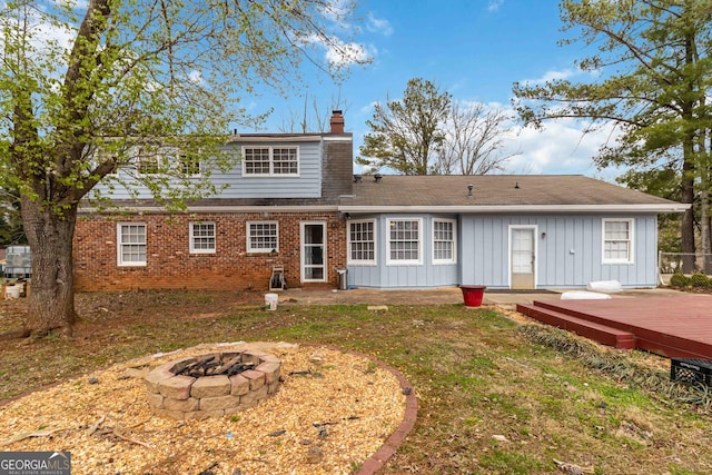 rear view of house featuring brick siding, a chimney, a fire pit, a deck, and board and batten siding