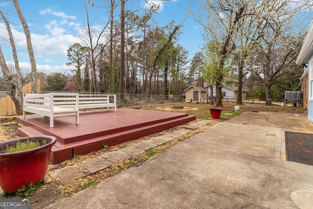 deck with a patio area, an outdoor structure, driveway, and fence