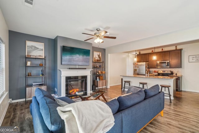 living room with visible vents, wood finished floors, baseboards, and a glass covered fireplace