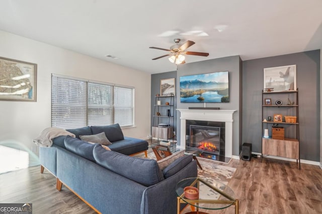 living area with a fireplace with flush hearth, baseboards, visible vents, and wood finished floors