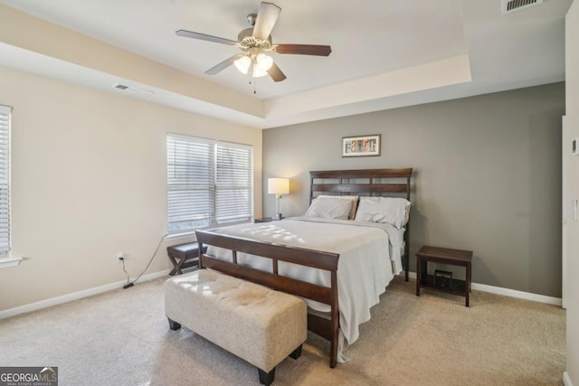 carpeted bedroom featuring a tray ceiling, baseboards, and visible vents