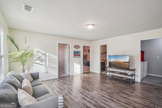 living area featuring wood finished floors, washing machine and dryer, visible vents, and baseboards