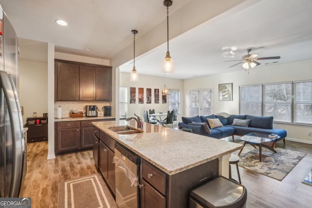 kitchen featuring backsplash, dark brown cabinetry, appliances with stainless steel finishes, wood finished floors, and a sink