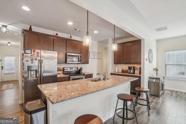 kitchen featuring wood finished floors, a sink, stainless steel appliances, a kitchen bar, and backsplash