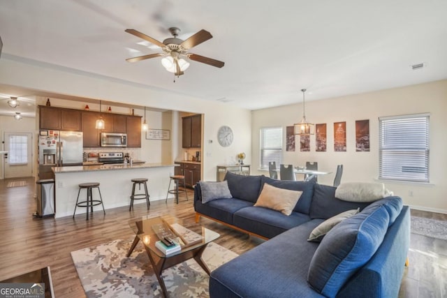 living area featuring visible vents, plenty of natural light, dark wood-type flooring, and a ceiling fan