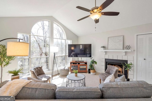 living area with a tiled fireplace, vaulted ceiling, carpet floors, and ceiling fan