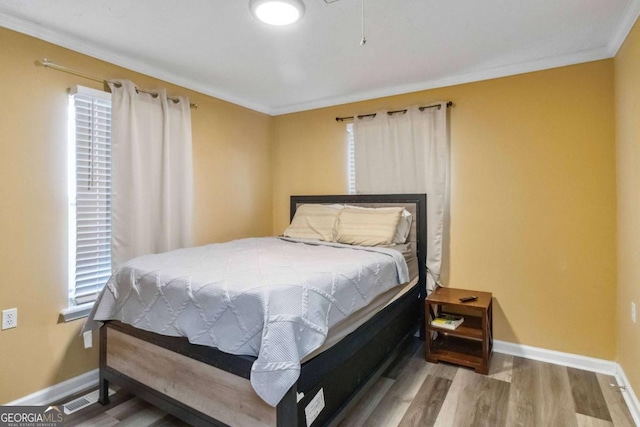 bedroom with visible vents, ornamental molding, baseboards, and wood finished floors