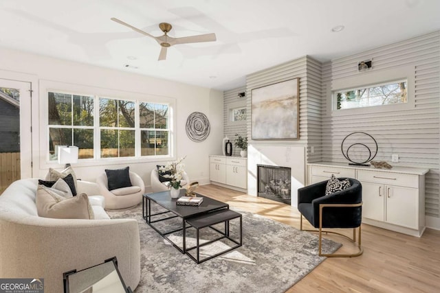 living area featuring a ceiling fan, plenty of natural light, light wood-style floors, and a fireplace