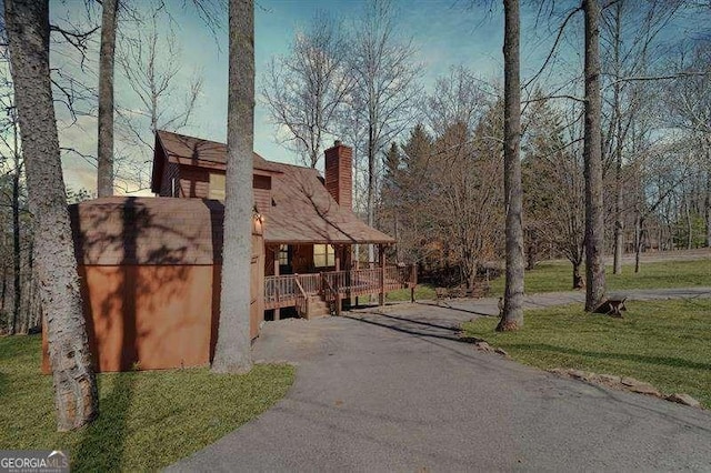 view of side of home featuring a porch, a lawn, aphalt driveway, and a chimney