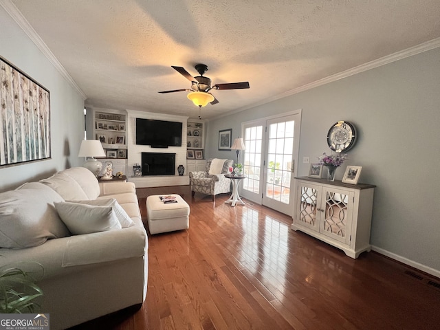 living area with built in features, wood finished floors, ceiling fan, a textured ceiling, and crown molding