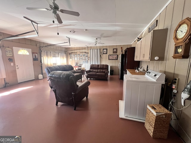 living room featuring a ceiling fan, washer and dryer, wood walls, a garage, and concrete flooring