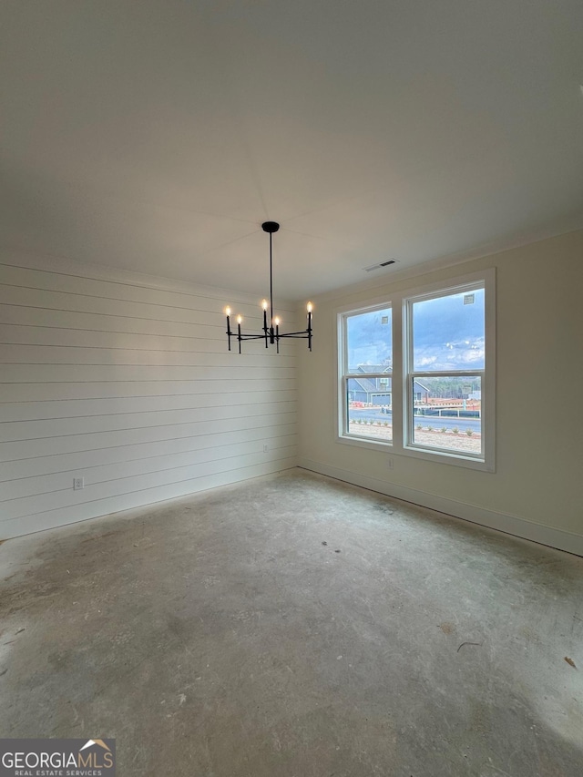 spare room featuring concrete floors and an inviting chandelier