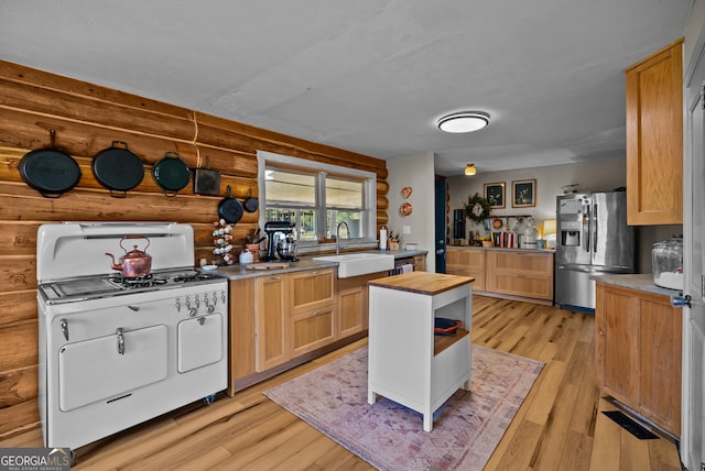 kitchen with light wood-type flooring, stainless steel refrigerator with ice dispenser, a sink, wooden counters, and white gas range