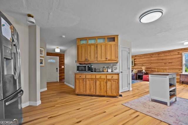 kitchen featuring baseboards, log walls, stainless steel appliances, glass insert cabinets, and light wood-style floors