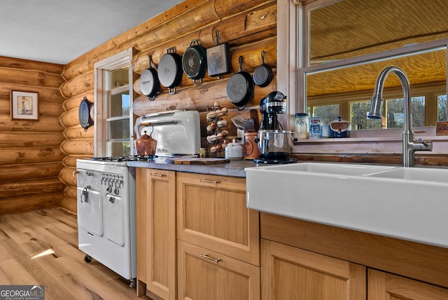 kitchen featuring light wood-type flooring, a sink, dark countertops, rustic walls, and gas stove