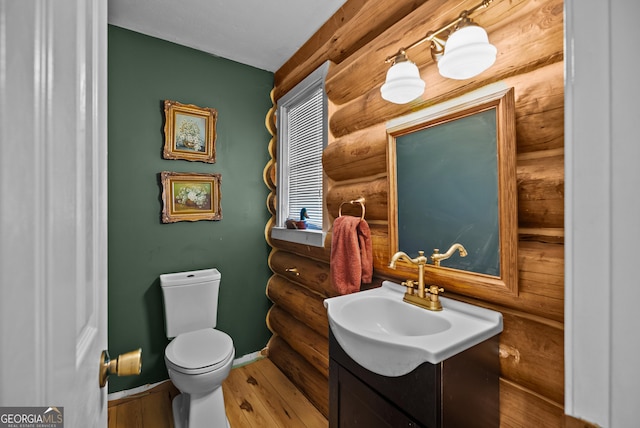 bathroom featuring toilet, wood finished floors, rustic walls, baseboards, and vanity