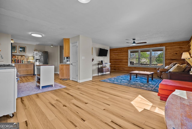 living room featuring rustic walls, light wood finished floors, baseboards, and a ceiling fan