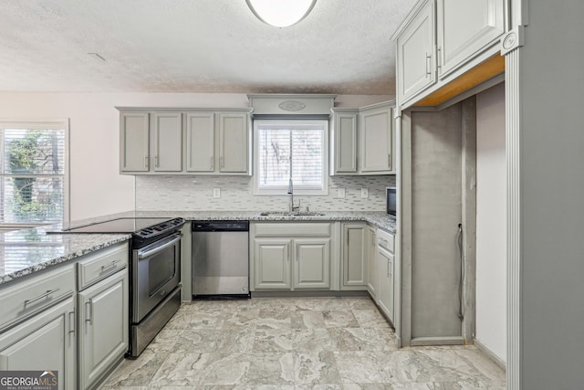 kitchen with light stone countertops, a sink, gray cabinetry, stainless steel appliances, and backsplash