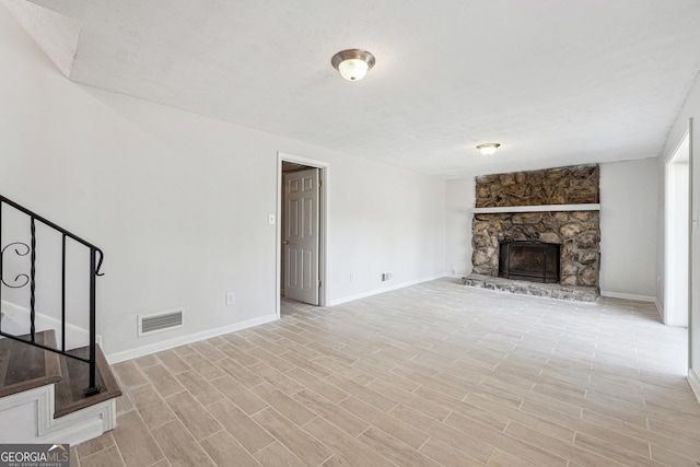 unfurnished living room featuring stairway, visible vents, baseboards, light wood-style flooring, and a stone fireplace