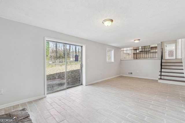 interior space with baseboards, visible vents, stairs, light wood-style floors, and a textured ceiling