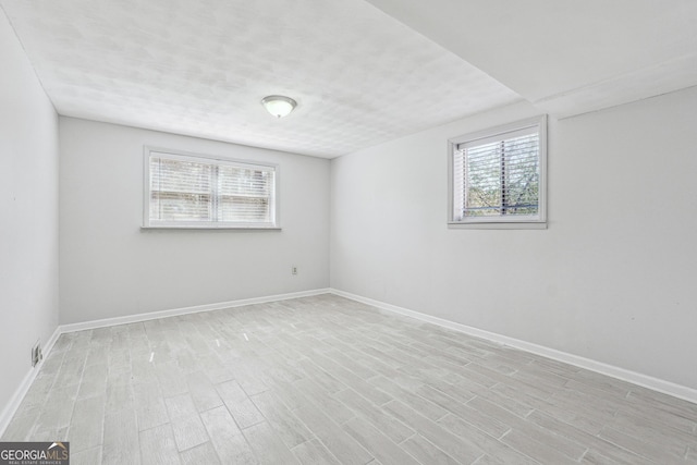 spare room with baseboards, plenty of natural light, and light wood finished floors