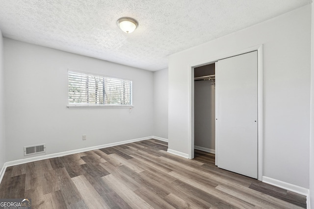 unfurnished bedroom with visible vents, baseboards, wood finished floors, a closet, and a textured ceiling