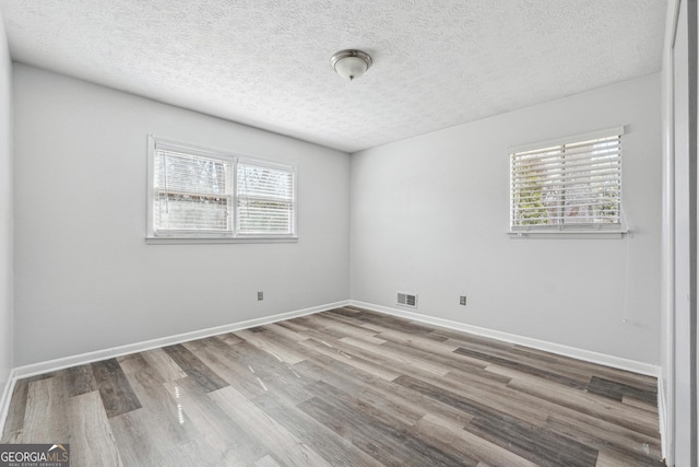 unfurnished room featuring visible vents, a textured ceiling, baseboards, and wood finished floors