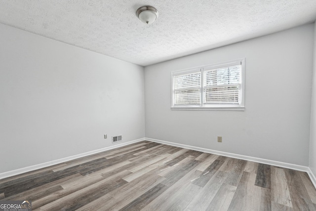 empty room with a textured ceiling, wood finished floors, visible vents, and baseboards