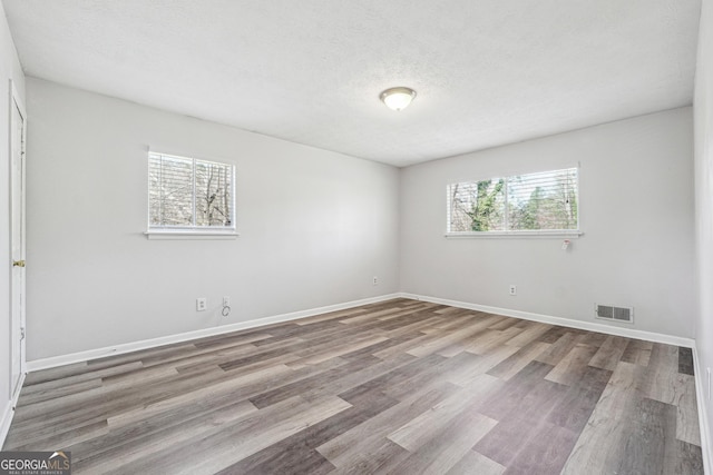 unfurnished room featuring visible vents, baseboards, a textured ceiling, and wood finished floors