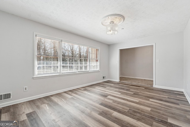 unfurnished room with a textured ceiling, wood finished floors, visible vents, and baseboards