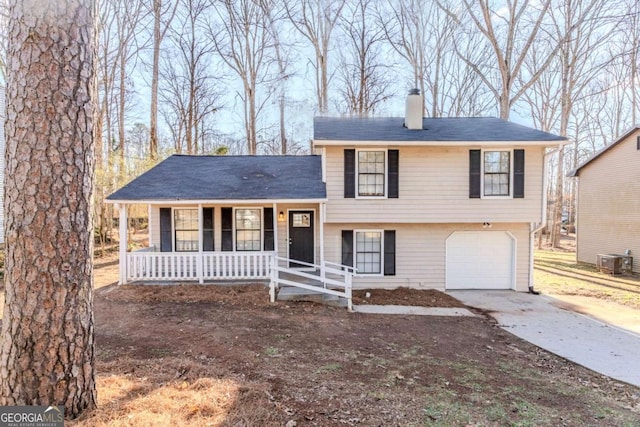 split level home with a porch, concrete driveway, central AC, a chimney, and an attached garage