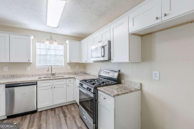 kitchen with a sink, a textured ceiling, white cabinetry, appliances with stainless steel finishes, and light wood finished floors