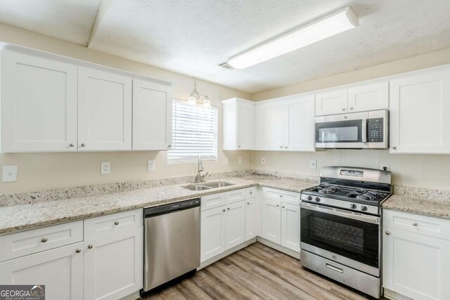 kitchen featuring light wood-type flooring, light stone counters, white cabinets, stainless steel appliances, and a sink