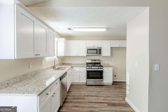 kitchen with light stone countertops, appliances with stainless steel finishes, wood finished floors, white cabinets, and a sink