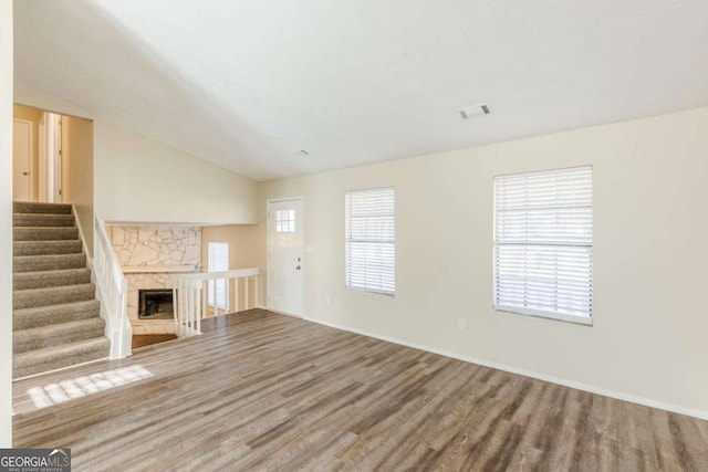 unfurnished living room with visible vents, stairway, lofted ceiling, a stone fireplace, and wood finished floors
