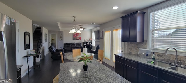 kitchen featuring dark stone countertops, a sink, pendant lighting, tasteful backsplash, and open floor plan