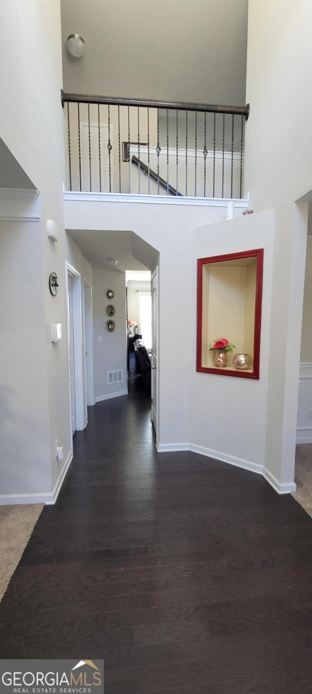 corridor with visible vents, baseboards, dark wood-type flooring, and a towering ceiling