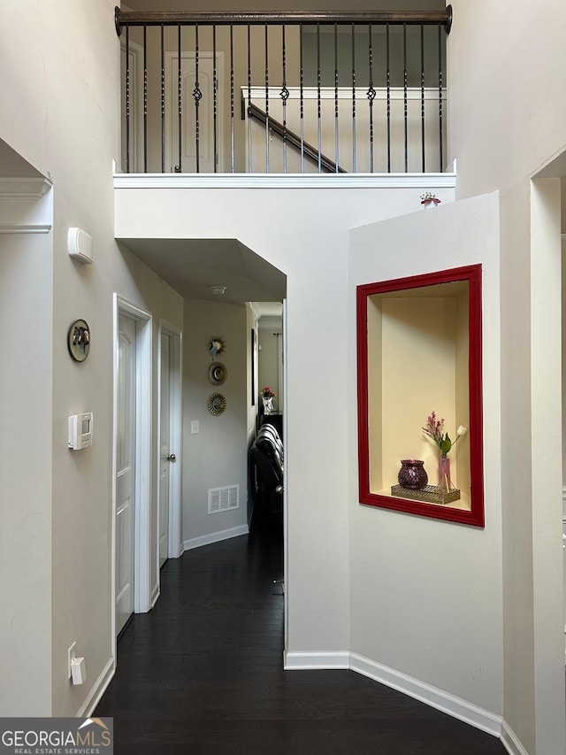 corridor featuring visible vents, baseboards, dark wood-type flooring, and a high ceiling