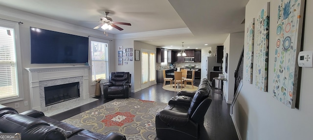 living area featuring baseboards, a high end fireplace, ceiling fan, ornamental molding, and dark wood-type flooring