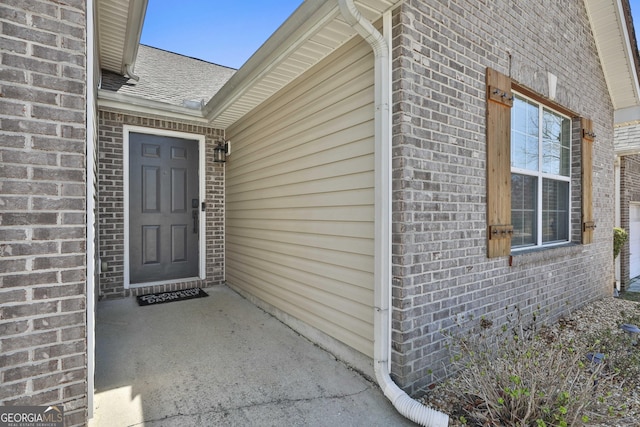 doorway to property featuring brick siding and a shingled roof