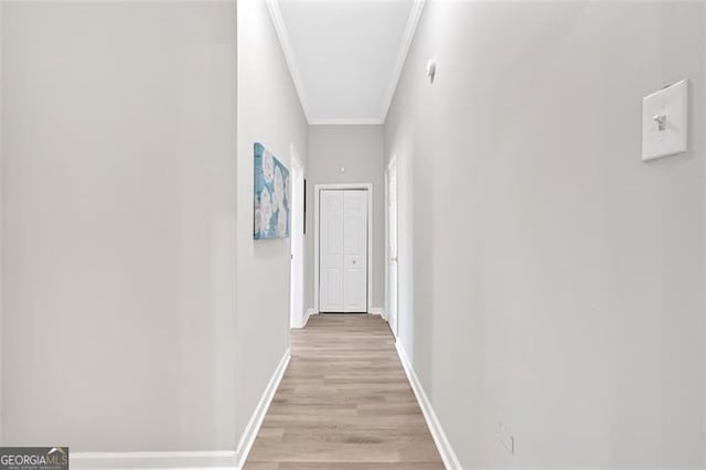 hall with light wood-type flooring, baseboards, and ornamental molding