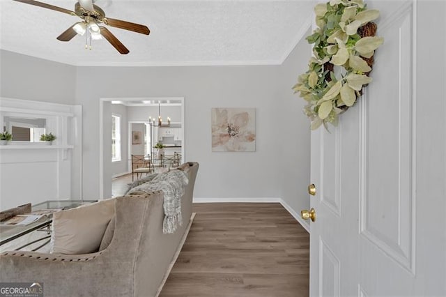 living room featuring baseboards, ornamental molding, ceiling fan with notable chandelier, wood finished floors, and a textured ceiling