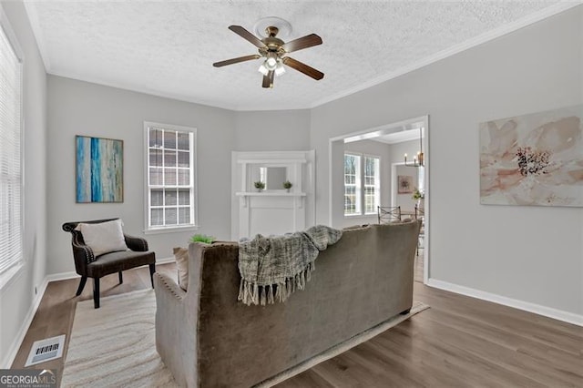 living room with visible vents, a textured ceiling, wood finished floors, and ornamental molding