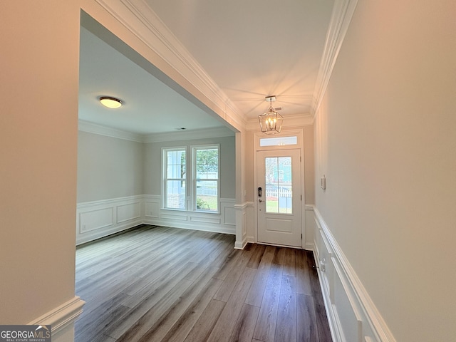 doorway featuring crown molding, dark wood-type flooring, wainscoting, a notable chandelier, and a decorative wall