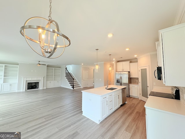 kitchen with a sink, a fireplace, hanging light fixtures, stainless steel appliances, and a kitchen island with sink