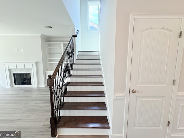 staircase with wood finished floors, baseboards, visible vents, a fireplace, and ornamental molding