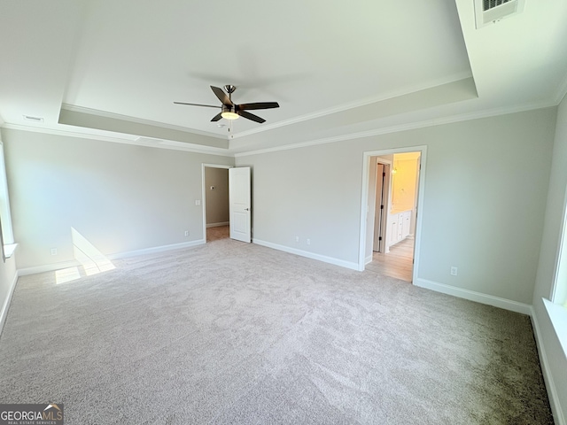 unfurnished bedroom featuring baseboards, visible vents, a tray ceiling, ornamental molding, and light carpet