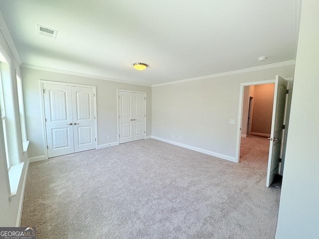 unfurnished bedroom with visible vents, two closets, crown molding, and carpet